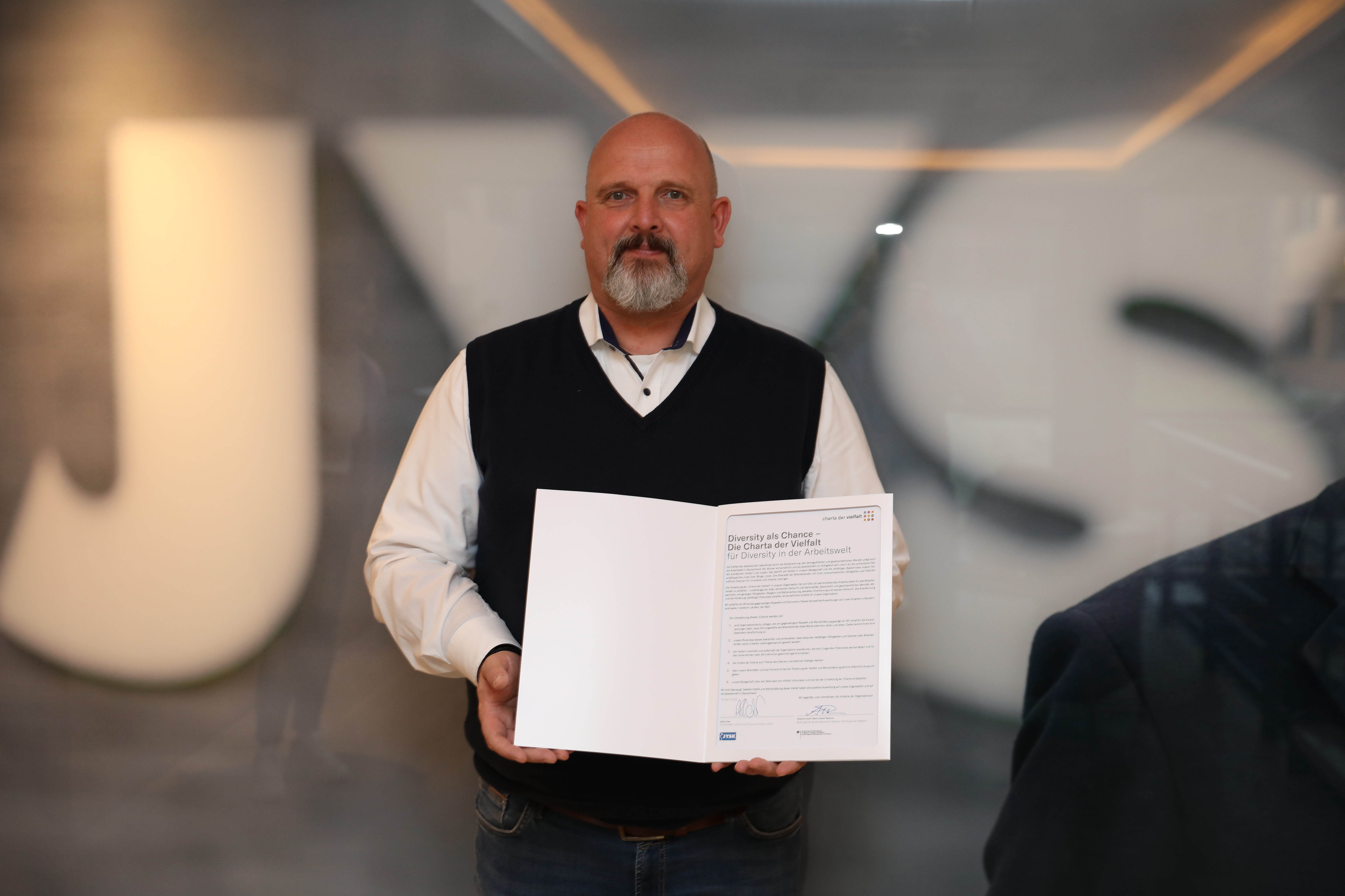 Ein Mann mit Bart hält eine Urkunde in der Hand 