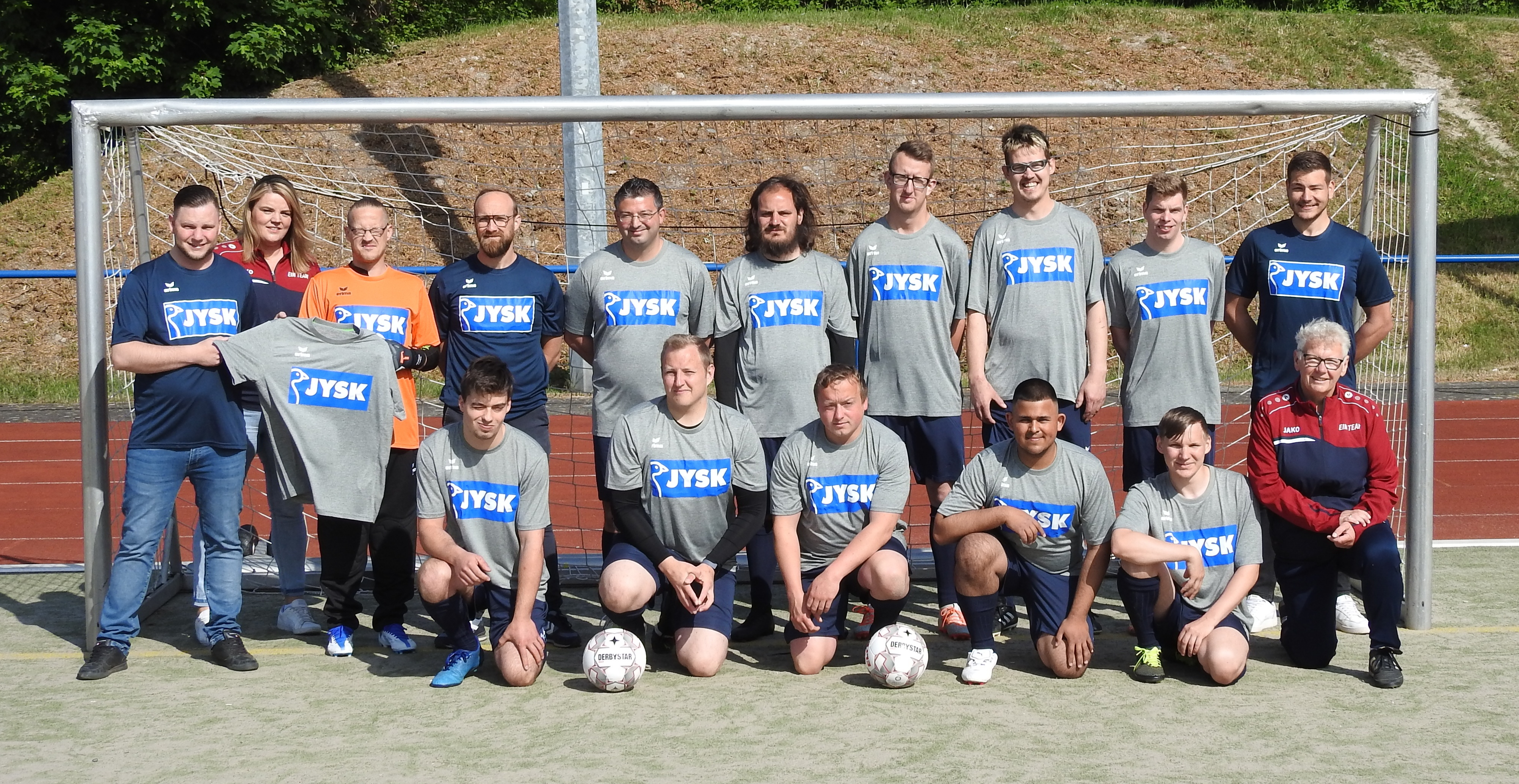 Viele Menschen, vor allem Männer, stehen vor einem Fußballtor, tragen neue Trikots und freuen sich.