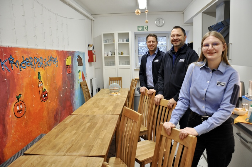 Zwei Männer und eine Frau in JYSK-Arbeitskleidung stehen in einer Küche und lächeln in die Kamera