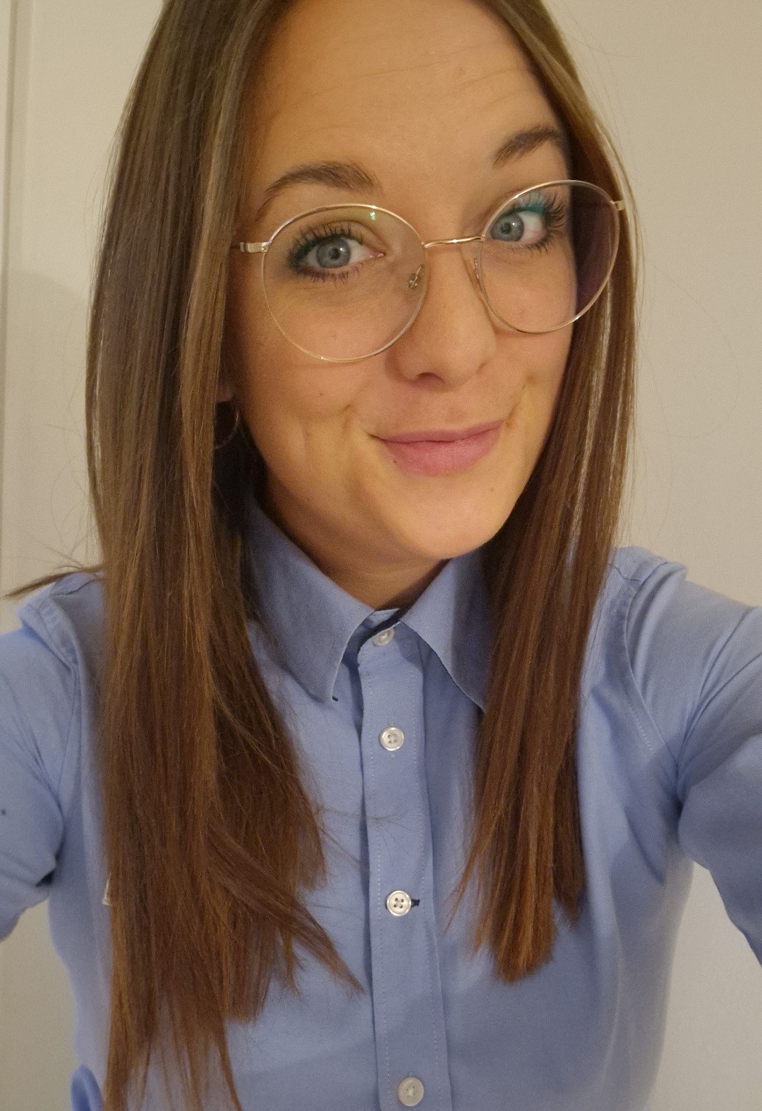 Eine junge Frau mit langen Haaren und Brille lächelt in eine Kamera. Sie trägt ein JYSK-Hemd