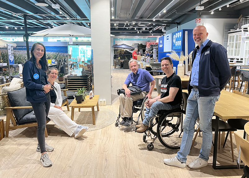 Fem personer står eller sitter i en halvmåneformad klunga och tittar mot kameran och ler. På vänster sida sett framifrån står ställföreträdande butikschef Linn Carlsson. bakom henne sitter Etableringschef Sara Winblad i en träsoffa. Mitt emot Linn står Store Concept Manager Sten Nielsen. Bredvid Sten sitter FIFH Malmös representanter Henrik Larsson och Peter Nilsson i vars en rullstol. I bakgrunden syns trädgårdsmöbler och kassadisken där en medarbetare tar betalt av en man i röd tröja.