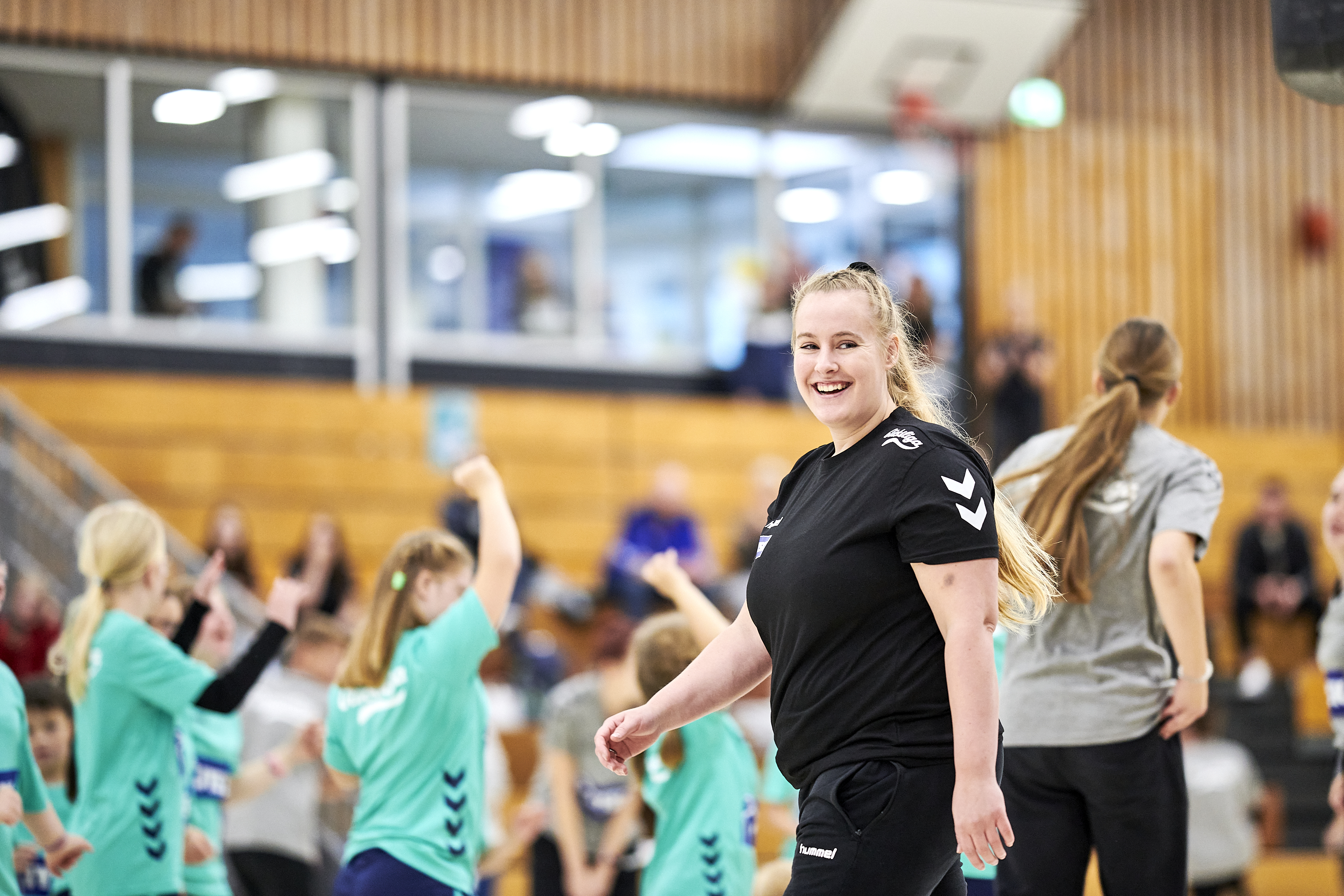 Eine junge Frau mit langem Pferdeschwanz läuft durch eine Sporthalle. Sie lächelt.