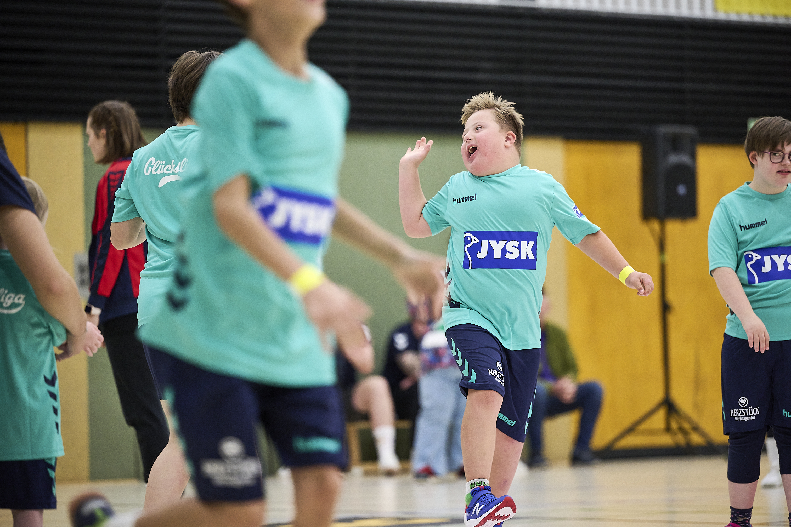Ein Junge läuft lachend durch eine Sporthalle. Er trägt ein Glücksliga-Trikot