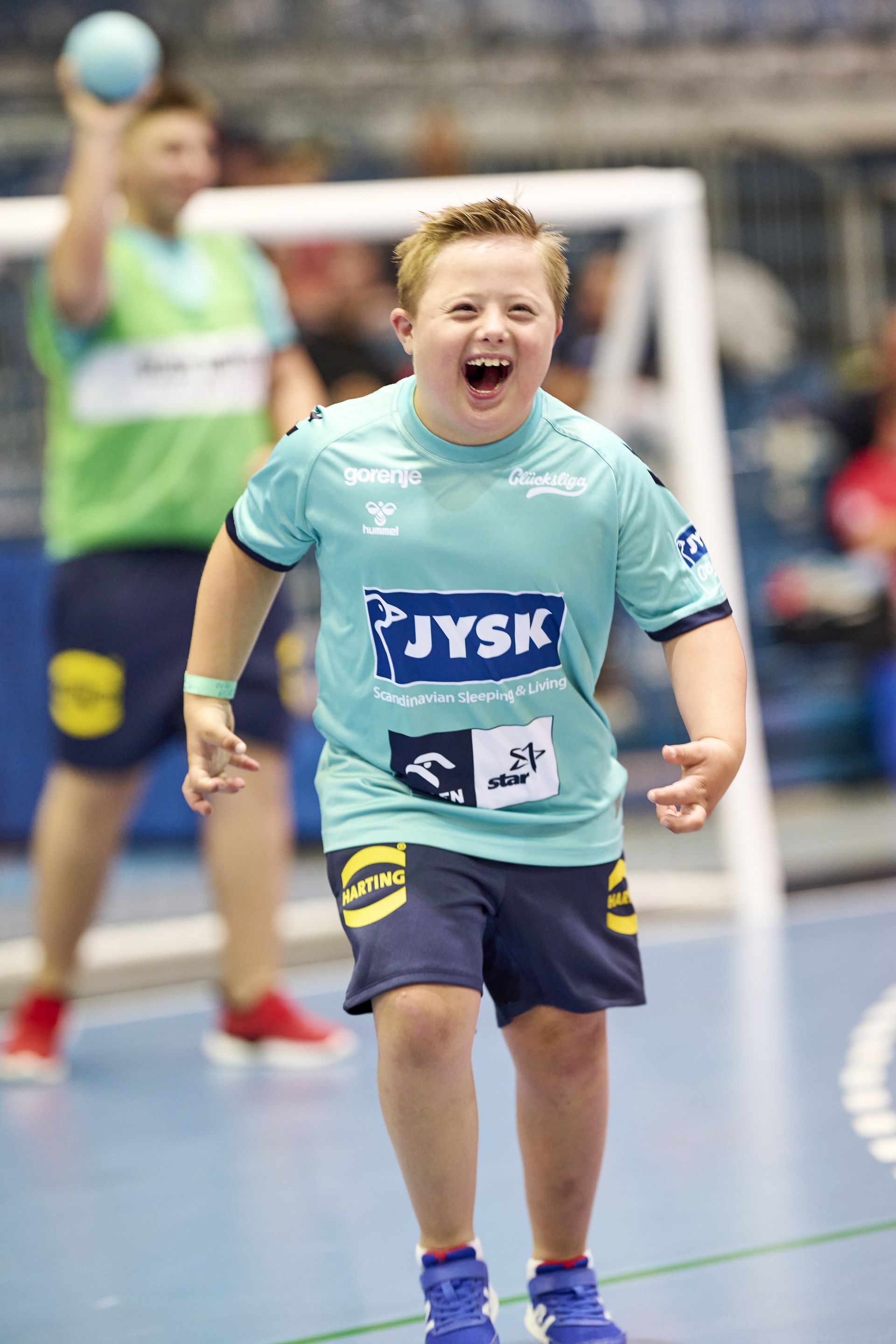 Ein Junge läuft lachend Richtung Kamera. Er trägt ein Trikot, auf dem der Schriftzug "JYSK" zu sehen ist.