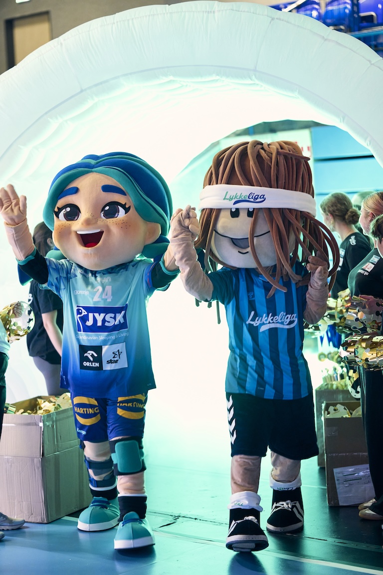 Zwei Maskottchen stehen in einer Turnhalle und winken