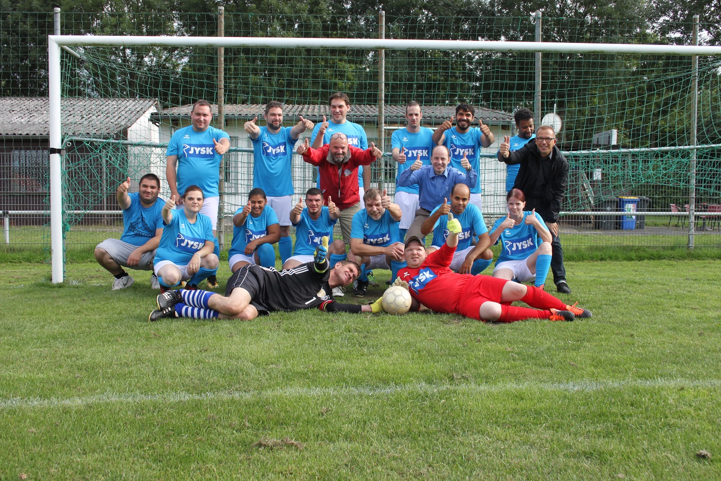 Viele Leute stehen vor einem Fußballtor, tragen neue Trikots und freuen sich. 