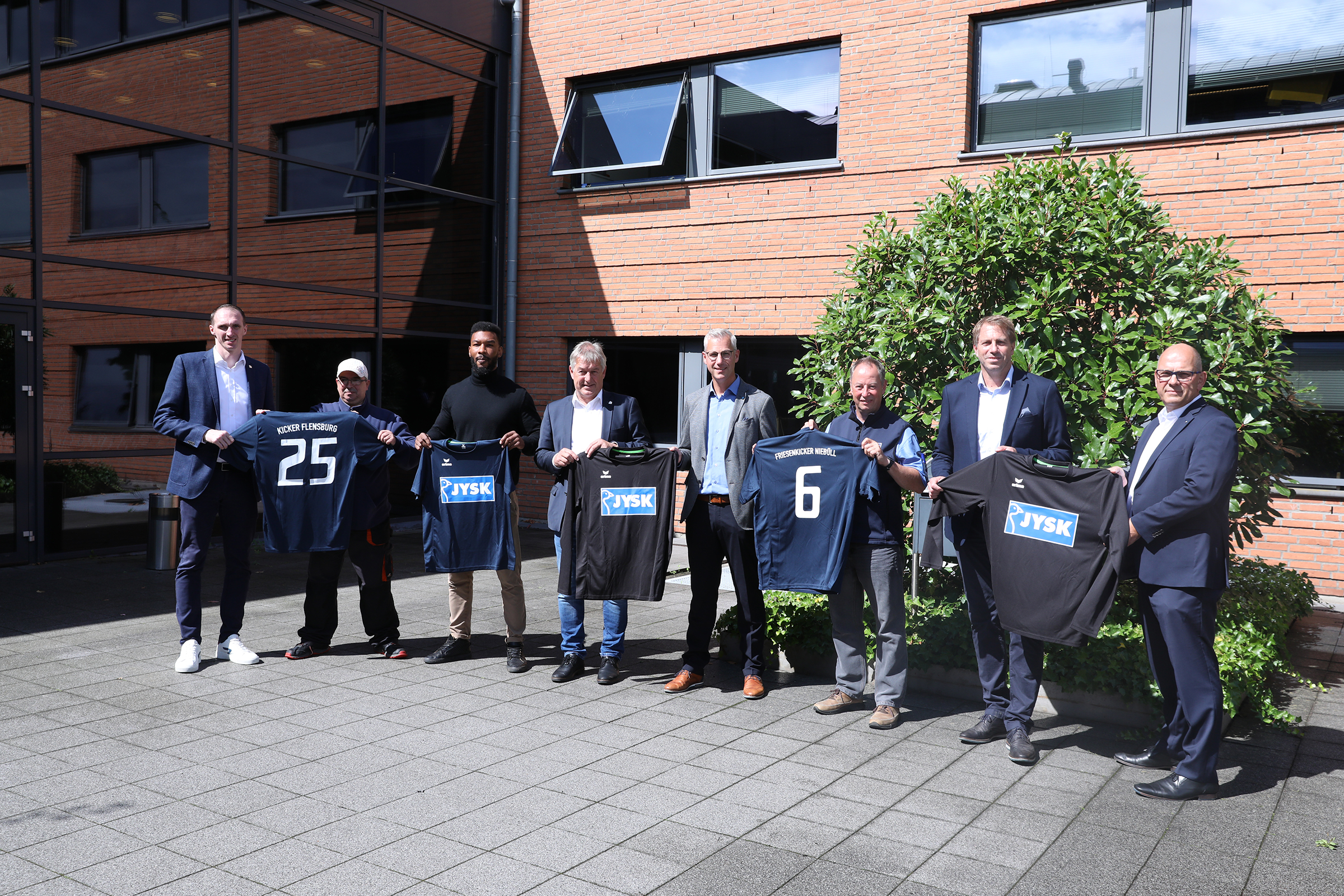 Mehrere Männer stehen vor dem Regional Head Office in Handewitt und halten Trikots in die Kamera