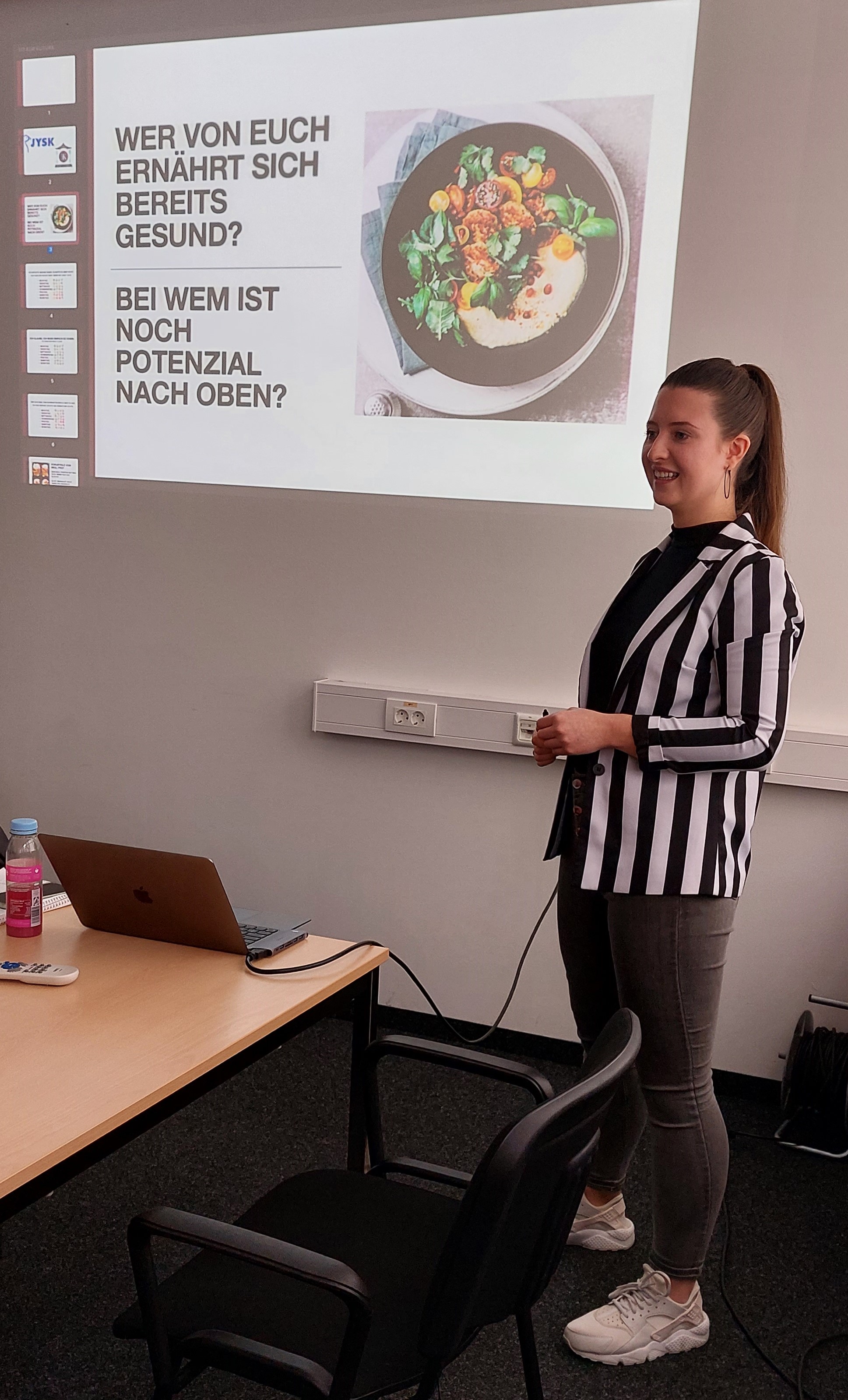 Eine Frau in Blazer steht vor einer Gruppe und erklärt etwas 