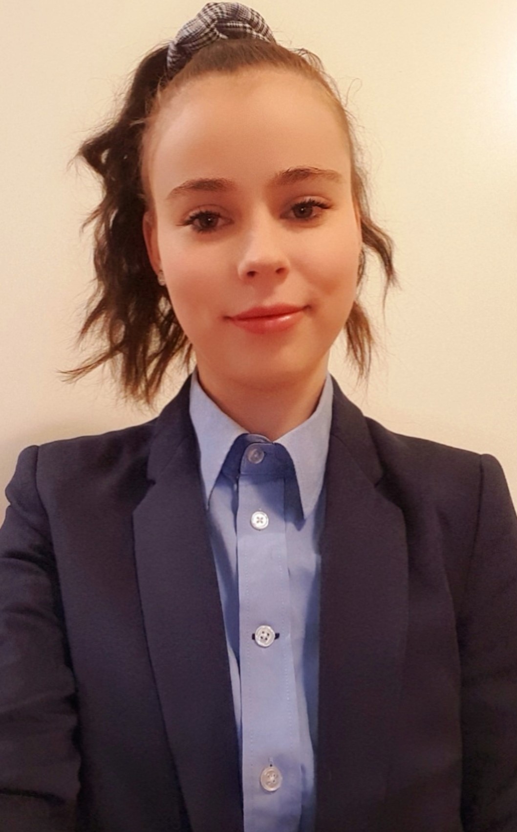Eine junge Frau mit Pferdeschwanz lächelt in die Kamera. Sie trägt einen Blazer mit JYSK-Hemd
