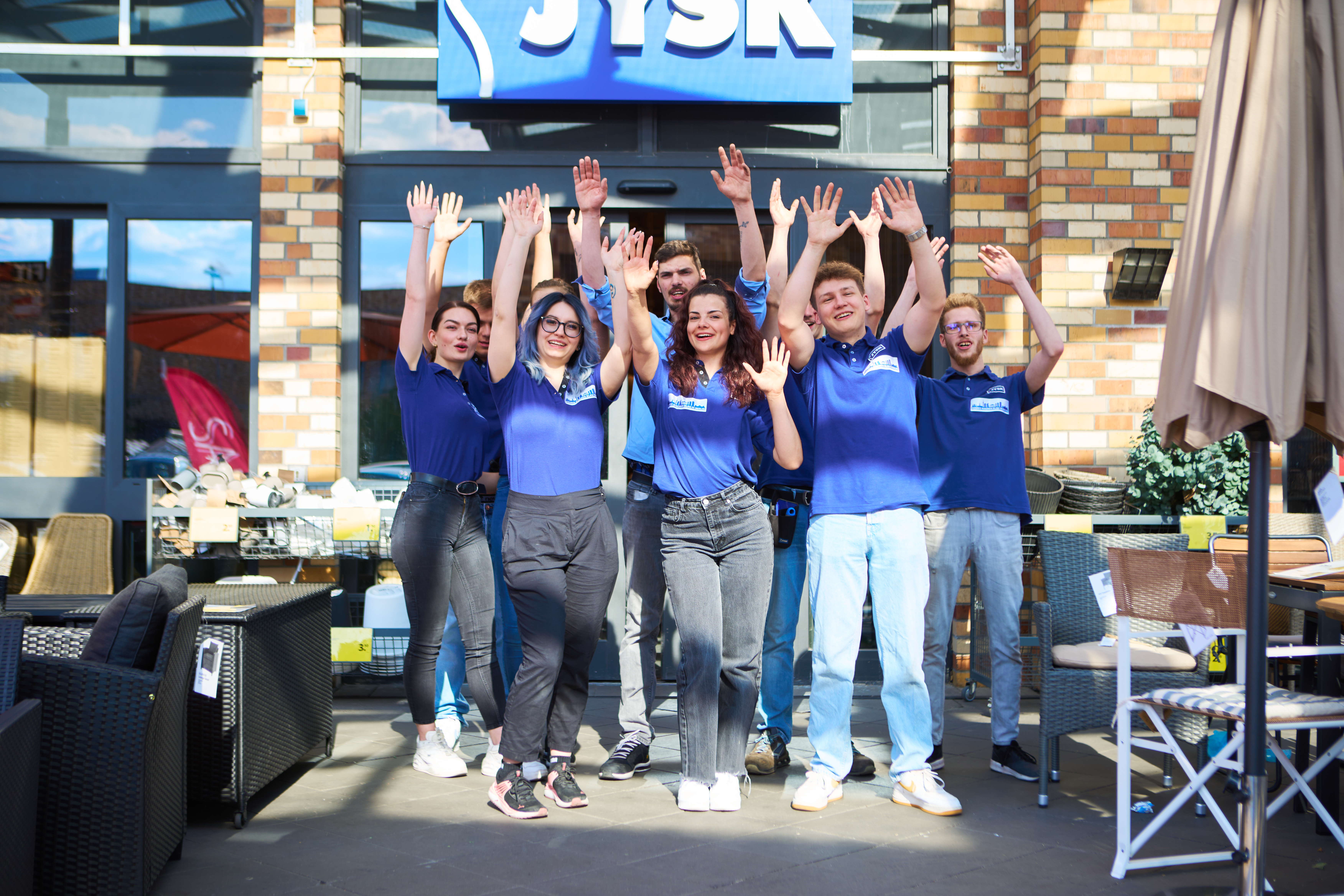 Jóvenes situados delante de una tienda JYSK y levantan los brazos en el aire