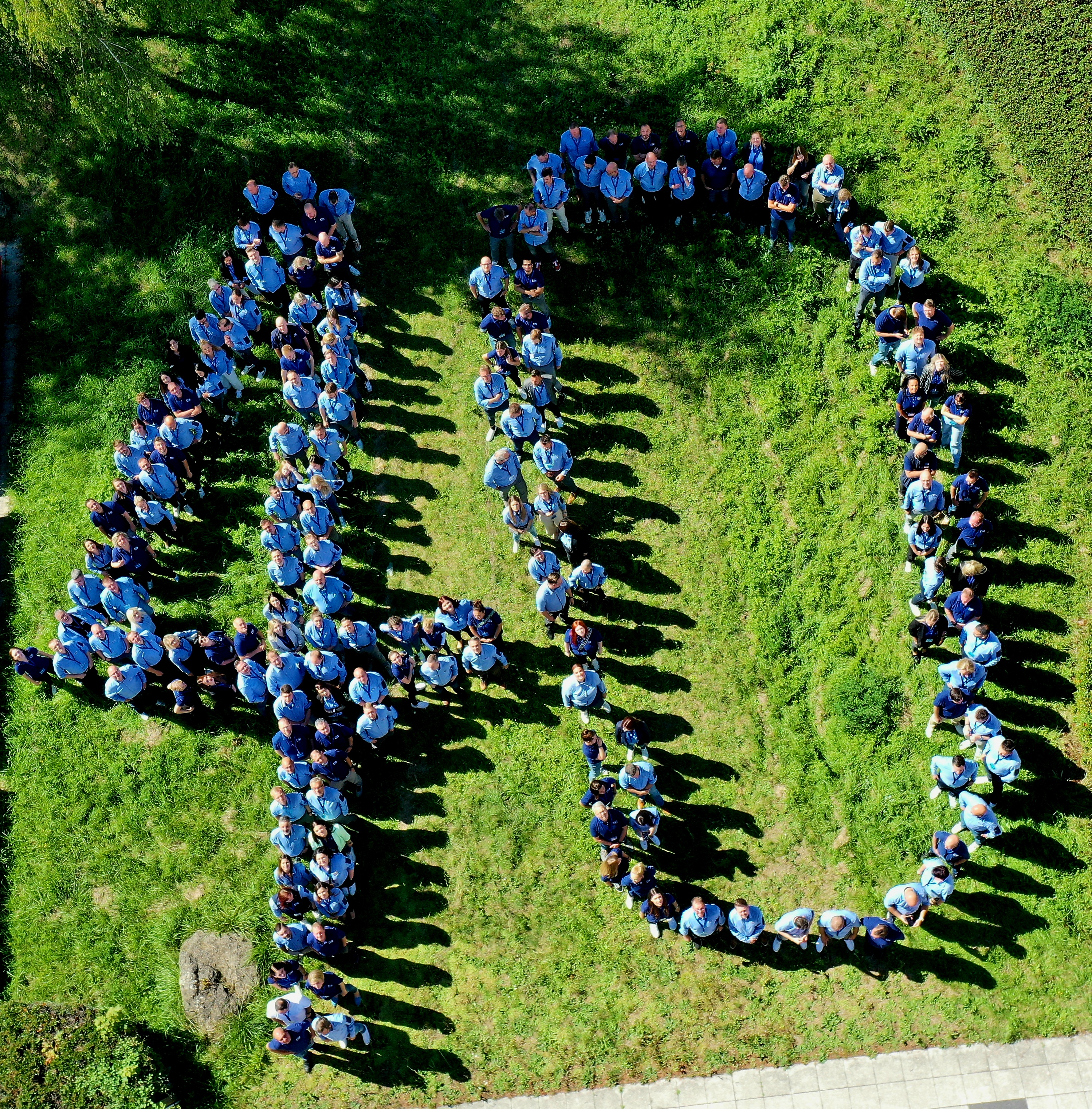 Zahlreiche Menschen in JYSK-Hemden und Poloshirts stehen auf einer wiese. Gemeinsam formen sie eine 40