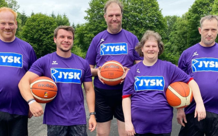 Fünf Menschen, eine Frau und vier Männer, stehen zusammen. In den Händen hält jede Person einen Basketball.