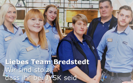 Fünf Personen – drei Frauen und zwei Männer – schauen in eine Kamera. Sie tragen JYSK-Hemden und Poloshirts