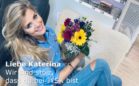 Eine junge Frau mit langen Haaren sitzt auf einem flauschigen Sessel. Sie hält einen Blumenstrauß in der Hand und lächelt in die Kamera