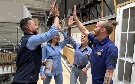 Fyra butikschefstraineer gör high five i butiksmiljö. 