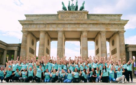 Mehr als 100 junge Menschen stehen vorm Brandenburger Tor – ein Tor, das auf sechs Säulen steht und sich mitten in Berlin befindet. Die Menschen haben die Arme hochgerissen und jubeln.
