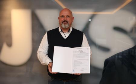 Ein Mann mit Bart hält eine Urkunde in der Hand 