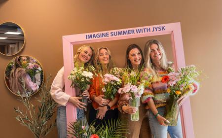 Four women standing with a frame and flowers smiling