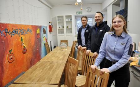 Zwei Männer und eine Frau in JYSK-Arbeitskleidung stehen in einer Küche und lächeln in die Kamera